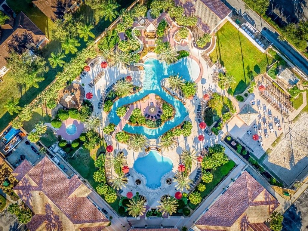 Vista aérea de un resort con una piscina central, rodeado de palmeras y tumbonas.