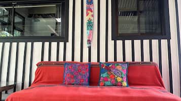 A bed with a red cover and two colorful pillows, against a wall with vertical black and white stripes.