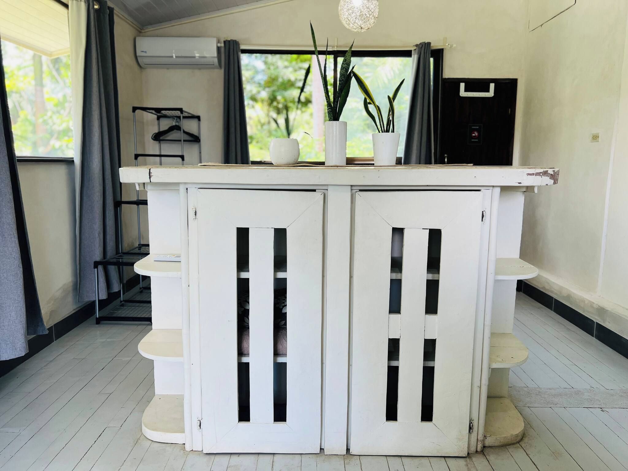 A white, two-door cabinet with shelves, a hanging light fixture, and a potted plant on top.