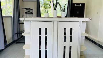 A white, two-door cabinet with shelves, a hanging light fixture, and a potted plant on top.