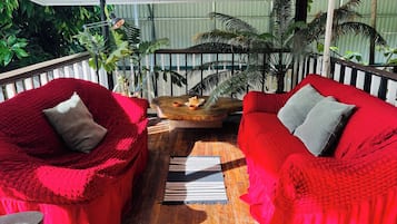 A covered outdoor seating area with two red cushioned chairs and a wooden table, surrounded by potted plants.