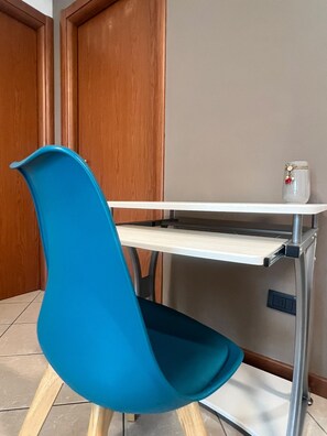 A room with a white desk, a blue chair, and a small white vase with a flower on the desk. - Strategically located near downtown Milan, Bocconi, San Siro, Assago, and Humanitas. (Rozzano)