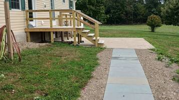 A house with a wooden deck and a concrete pathway leading to a grassy yard.