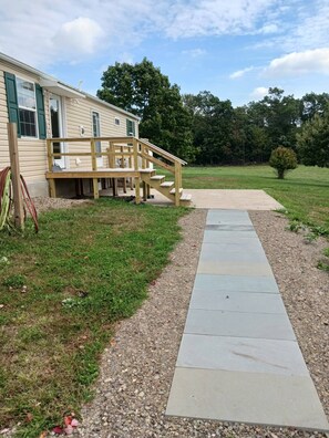A house with a wooden deck and a concrete pathway leading to a grassy yard.