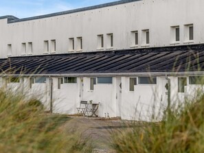 Un bâtiment doté de nombreuses fenêtres, d’un toit plat et d’un petit espace extérieur aménagé pour s’asseoir.