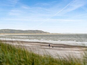 Une plage où l’on voit une personne qui se promène, des vagues et une colline au loin.