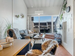 A modern living room with a sofa, a dining table, and a coffee table. There is a large window providing a view of the outside. - "Alena" - 50m from the sea by Interhome (Brovst)