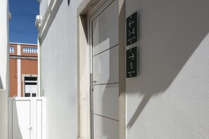 Ein Gebäudeeingang mit einer weißen Tür und einem an der Wand befestigten Schild, das die Zimmernummern 1 bis 4 und 5 anzeigt.