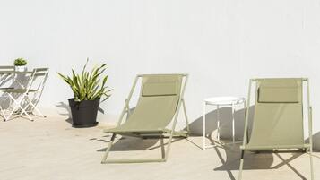 Trois chaises de jardin vertes et une petite table sont placées contre un mur blanc, avec une plante en pot à proximité.