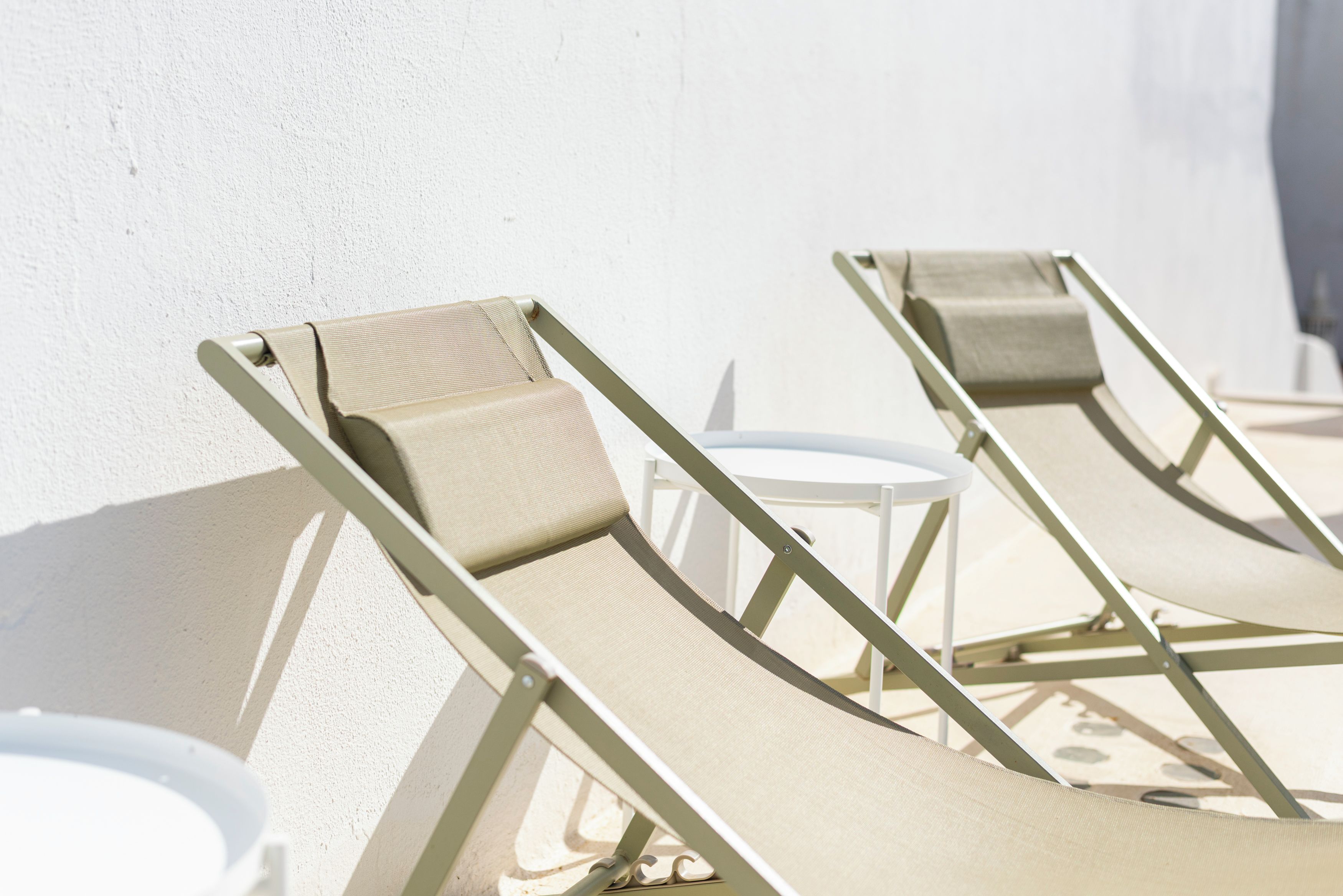 A row of sun loungers with a white wall and a small round table in the background.