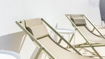 A row of sun loungers with a white wall and a small round table in the background.