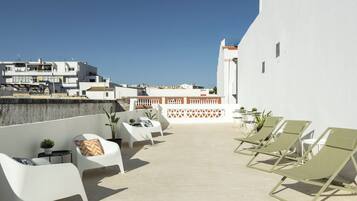 A rooftop terrace with white lounge chairs, a small table, and potted plants.