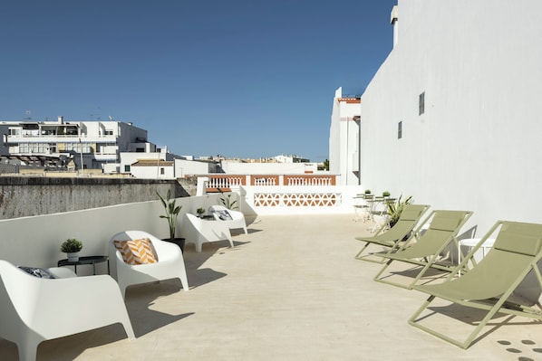 A rooftop terrace with white lounge chairs, a small table, and potted plants.