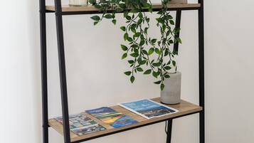 Une étagère en métal avec une plante, une bougie et des brochures.