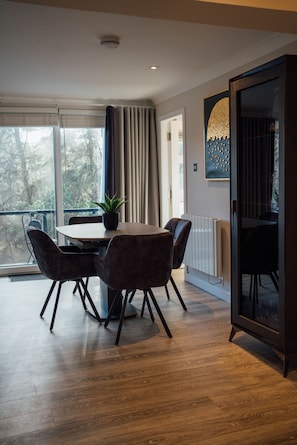 Ein moderner Essbereich mit Tisch, Stühlen, einem Blumentopf und Blick auf Bäume durch das Fenster.