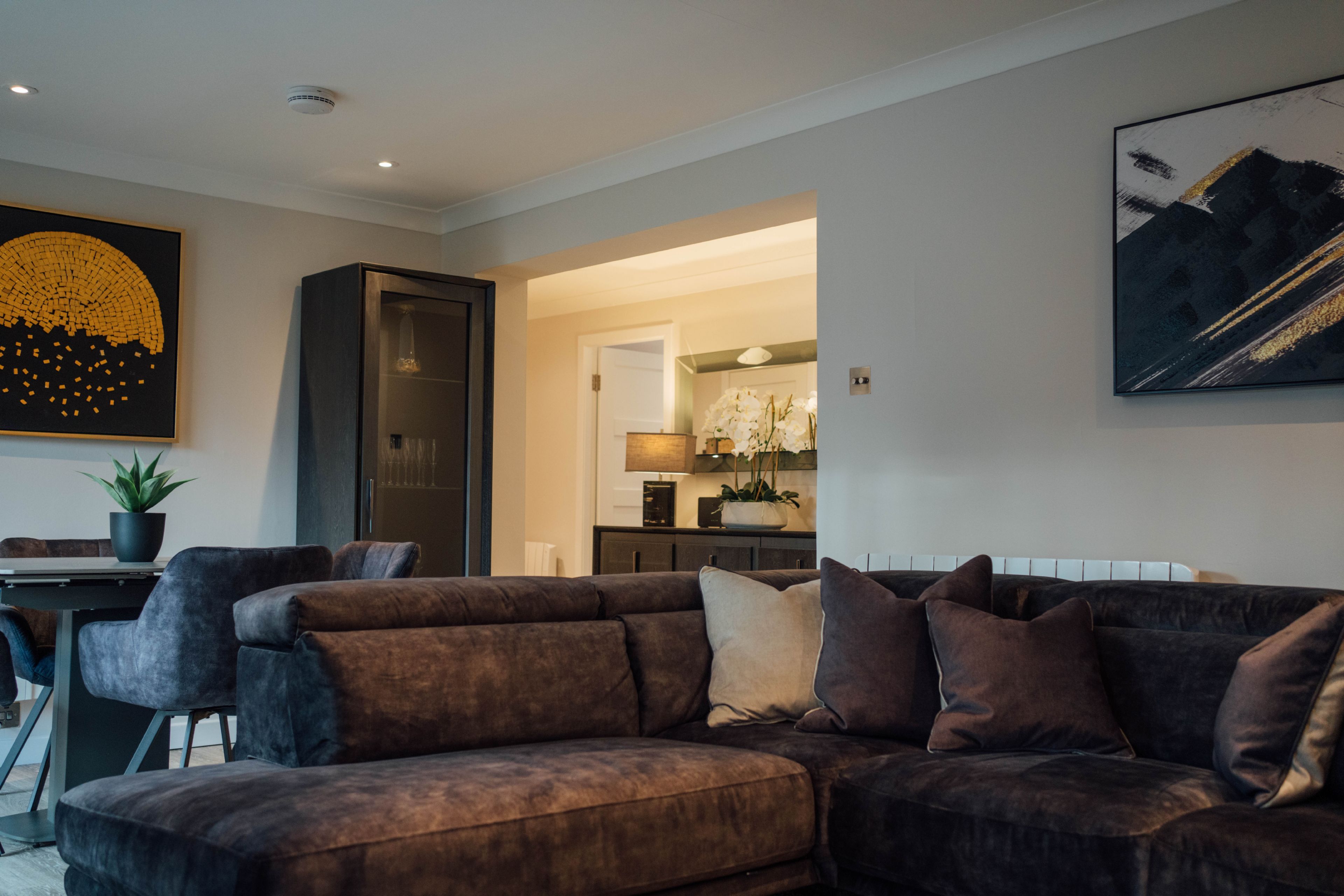 A modern living room with a sectional sofa, a dining area with a table and chairs, and a kitchen in the background.