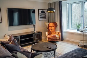 Ein modernes Wohnzimmer mit Flachbildfernseher, Spielkonsole, Couchtisch und einem einzigartigen Designstuhl.