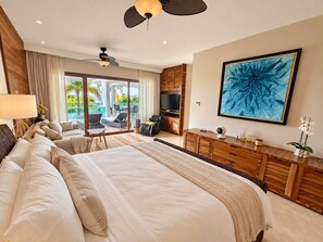 A spacious bedroom with a large bed, a ceiling fan, a television, and a balcony with outdoor seating. - Luxury Peninsula Condo with Canal and Ocean Views / Newly Renovated / 3 Bedrooms (Puerto Aventuras)