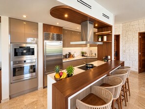 A modern kitchen with stainless steel appliances, a wooden island, and a stone wall. - Luxury Peninsula Condo with Canal and Ocean Views / Newly Renovated / 3 Bedrooms (Puerto Aventuras)