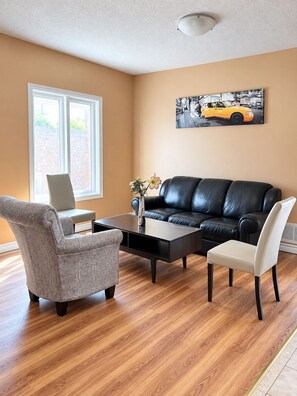 A living room with a black leather sofa, two armchairs, a coffee table, and a laptop on a grey armchair. - Private Queen Bedroom w/ Workspace & Dresser, 2.5 Bath—Shared Home (Brampton)