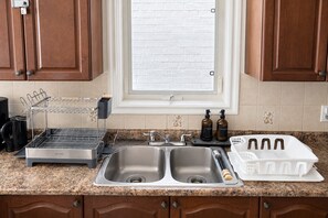 A kitchen with a double sink, a dish drying rack, a coffee maker, and a window with a view. - Private Queen Bedroom w/ Workspace & Dresser, 2.5 Bath—Shared Home (Brampton)