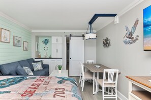 Ein Zimmer mit einem Bett, einem Schreibtisch, einem Stuhl, einem Tisch und einer Essecke. Eine Tür führt in einen weiteren Raum.