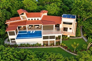 A modern multi-story house with a swimming pool, surrounded by lush greenery. - Casa de Shanti: Private Ocean-View 4BR Retreat with Infinity Pool & Hot Tub (Coco)