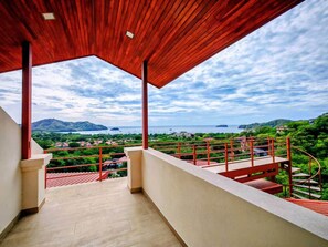 Ein Balkon mit Blick auf eine Küstenlandschaft, einer Holzbalkendecke und einem roten Geländer.