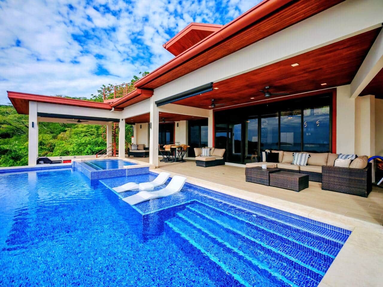 A modern outdoor pool area with a clear blue pool, lounge chairs, and a covered seating area.