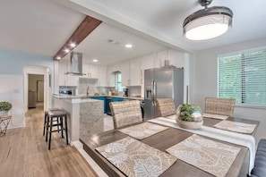 A modern kitchen with white cabinets, a stainless steel refrigerator, and a dining area with a table set for four. - Huge 7BR Beach Duplex – Walk to Sand & Surf (Daytona Beach)