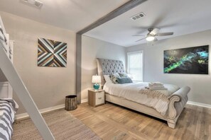 A bedroom with a bed, a nightstand, a lamp, a ceiling fan, and artwork on the walls. - Huge 7BR Beach Duplex – Walk to Sand & Surf (Daytona Beach)