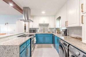 Una cocina con gabinetes blancos, una isla azul, electrodomésticos de acero inoxidable y un salpicadero de azulejos tipo espiga.