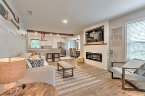 A modern living room with a fireplace, a television, and a dining area in the background. - Huge 7BR Beach Duplex – Walk to Sand & Surf (Daytona Beach)