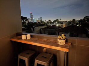 Un balcon avec une table en bois, deux tabourets et un pot de fleurs.