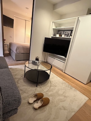 Ein modernes Wohnzimmer mit einer Couch, einem Couchtisch, Hausschuhen, einem Fernseher und einem weißen Schrank.