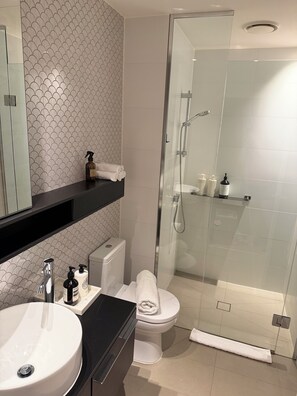 Une salle de bain moderne avec une douche à parois de verre, des toilettes blanches et un lavabo doté d’un plan de travail noir.