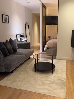 Ein modernes Wohnzimmer mit einer Couch, einem Glastisch und einem Bett im Hintergrund.