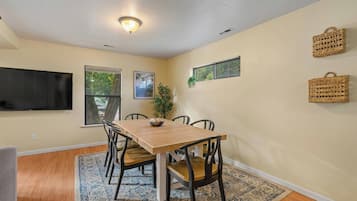 A dining area with a wooden table, chairs, a rug, and a television mounted on the wall.