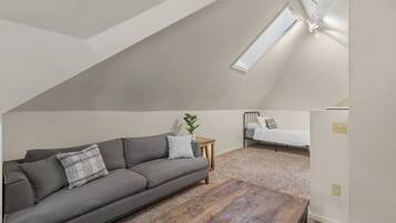 A loft bedroom with a sloped ceiling, a gray sofa, a wooden coffee table, a small bedside table, and a bed.