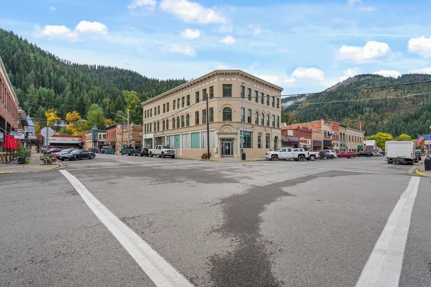 A town square with a prominent building, various vehicles, and a mountainous backdrop.