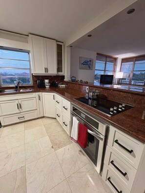 A modern kitchen with white cabinetry, a stainless steel stove, and a large window offering a view. - Sunny 2BR/2BA Waterfront Corner Apt Canal Views, Mins to Beach & Aventura (North Miami Beach)