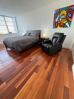 A bedroom with a bed, a chair, a nightstand, and a painting on the wall. - Sunny 2BR/2BA Waterfront Corner Apt Canal Views, Mins to Beach & Aventura (North Miami Beach)