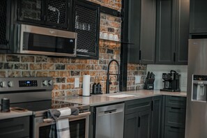 A modern kitchen with a brick wall, stainless steel appliances, and dark cabinetry. - "Rest & Redeem" New Luxury Cabin in Broken Bow (Broken Bow)