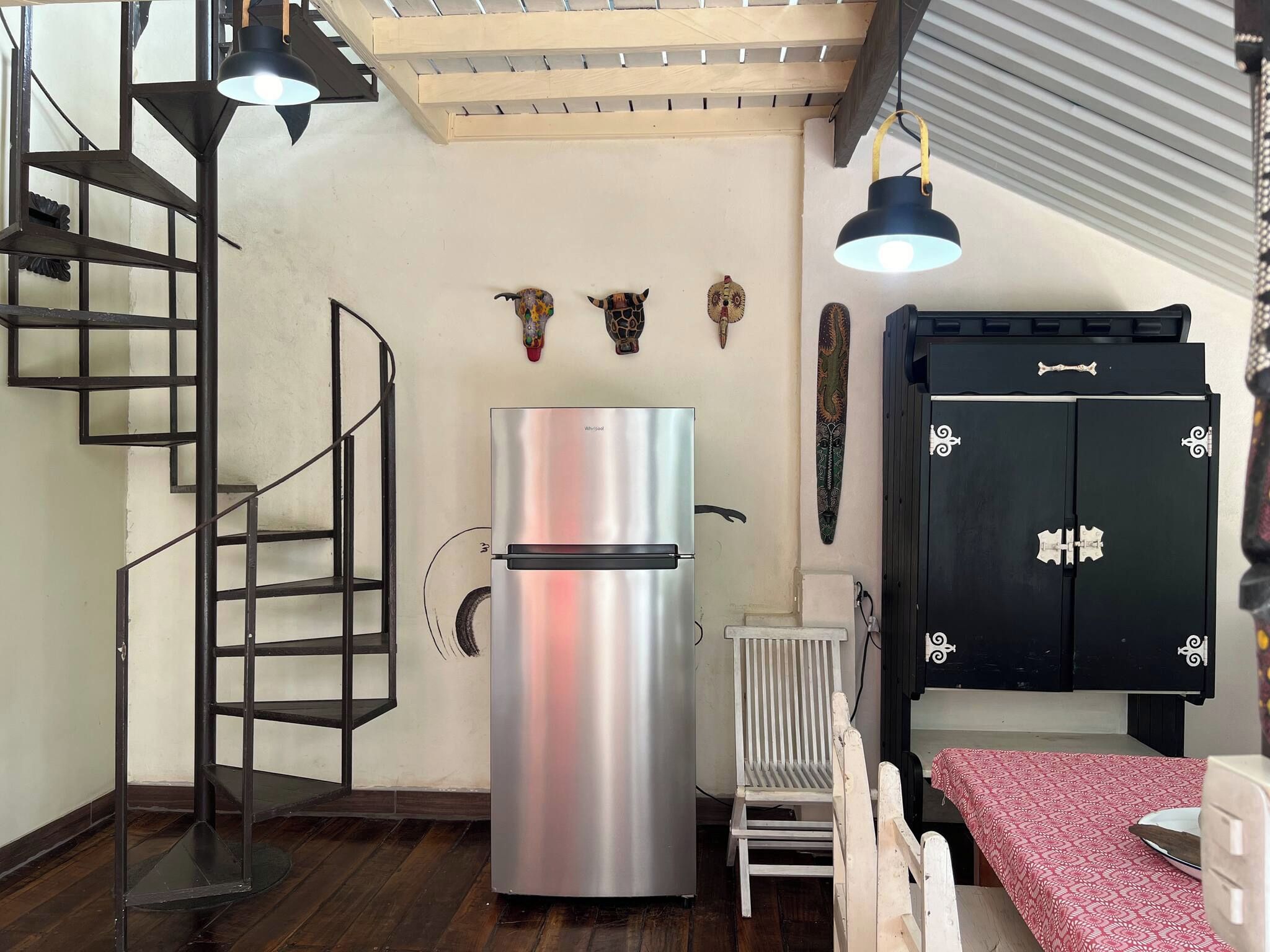 Une cuisine compacte dotée d’un réfrigérateur en acier inoxydable, d’un meuble noir agrémenté de poignées décoratives, d’un escalier en bois et d’un radiateur.