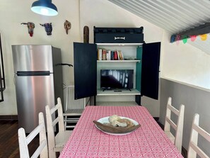 A compact living space with a kitchenette, a dining table with a patterned tablecloth, a refrigerator, a television, and a bookshelf. - Private Jungle Loft in Playa Cocles (Cahuita)