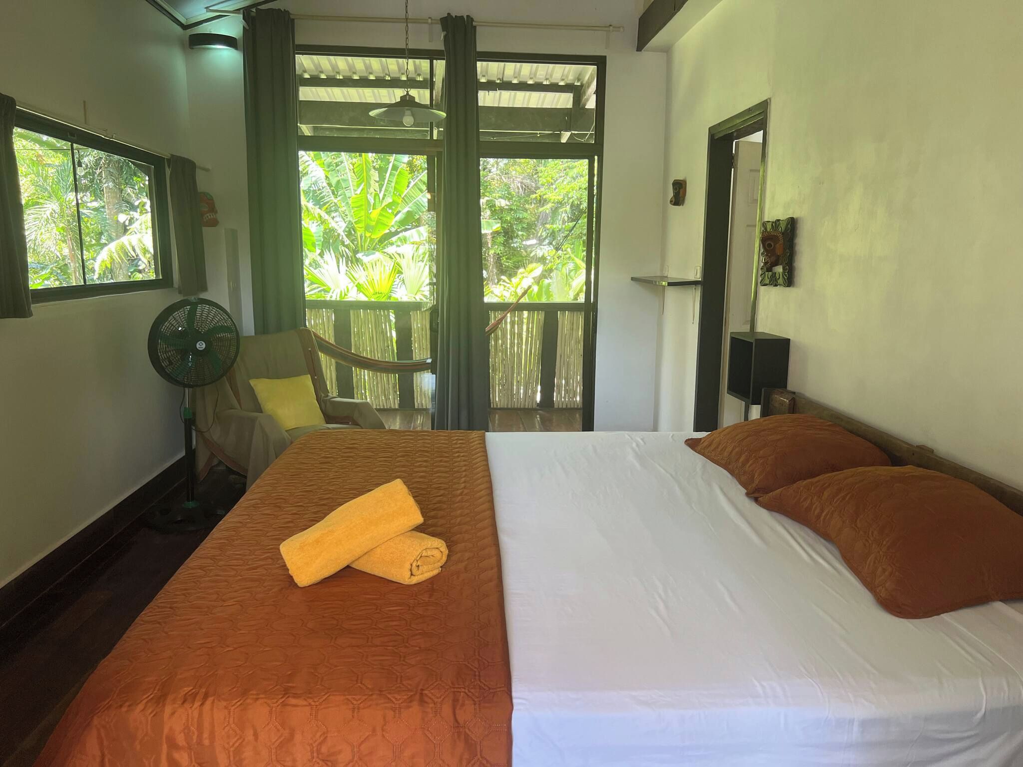 Une chambre à coucher avec un lit, un ventilateur, une chaise et une vue sur la verdure environnante.