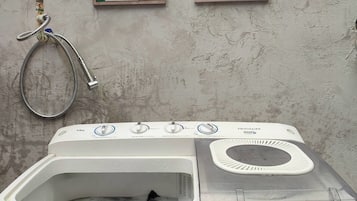 Una lavadora de carga frontal con un panel de control, una manguera y dos carteles informativos en la pared.