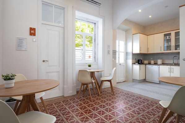 Una cocina limpia y moderna con armarios blancos, una zona de comedor con mesa y sillas, y baldosas de suelo estampadas.