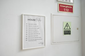 A wall with a framed list of house rules, a red emergency sign, and a door with a warning sign. - Casa Dona Irene Sunny Terrace | Room 1 | Early or Late Check-in (Faro)