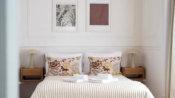 A hotel room with a bed, two nightstands, a radiator, and two framed pictures on the wall.